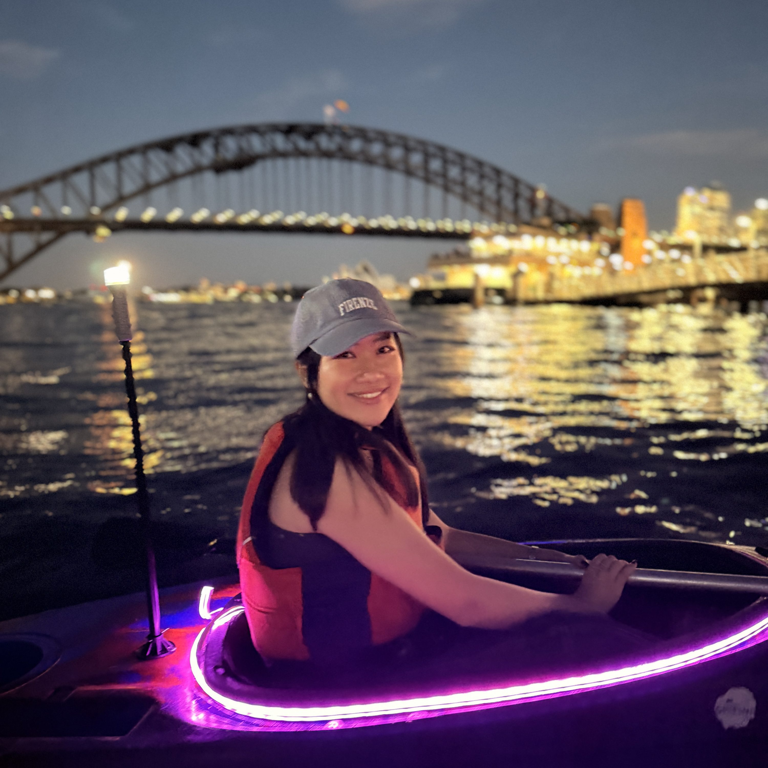 Pink LED kayaks glowing on Sydney Harbour after dark with the Sydney Harbour Bridge lit up