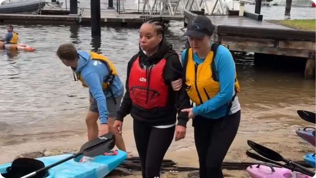Sydney By Kayak guides supporting a vision-impaired paddler arm in arm across the beach at Lavender Bay
