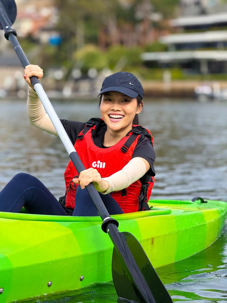 Lady kayaking in a green kayak and smiling at camera