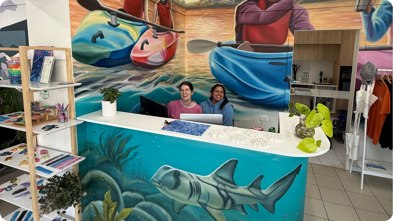 Team members at the Eco Hub reception desk surrounded by hand-painted kayaking murals.