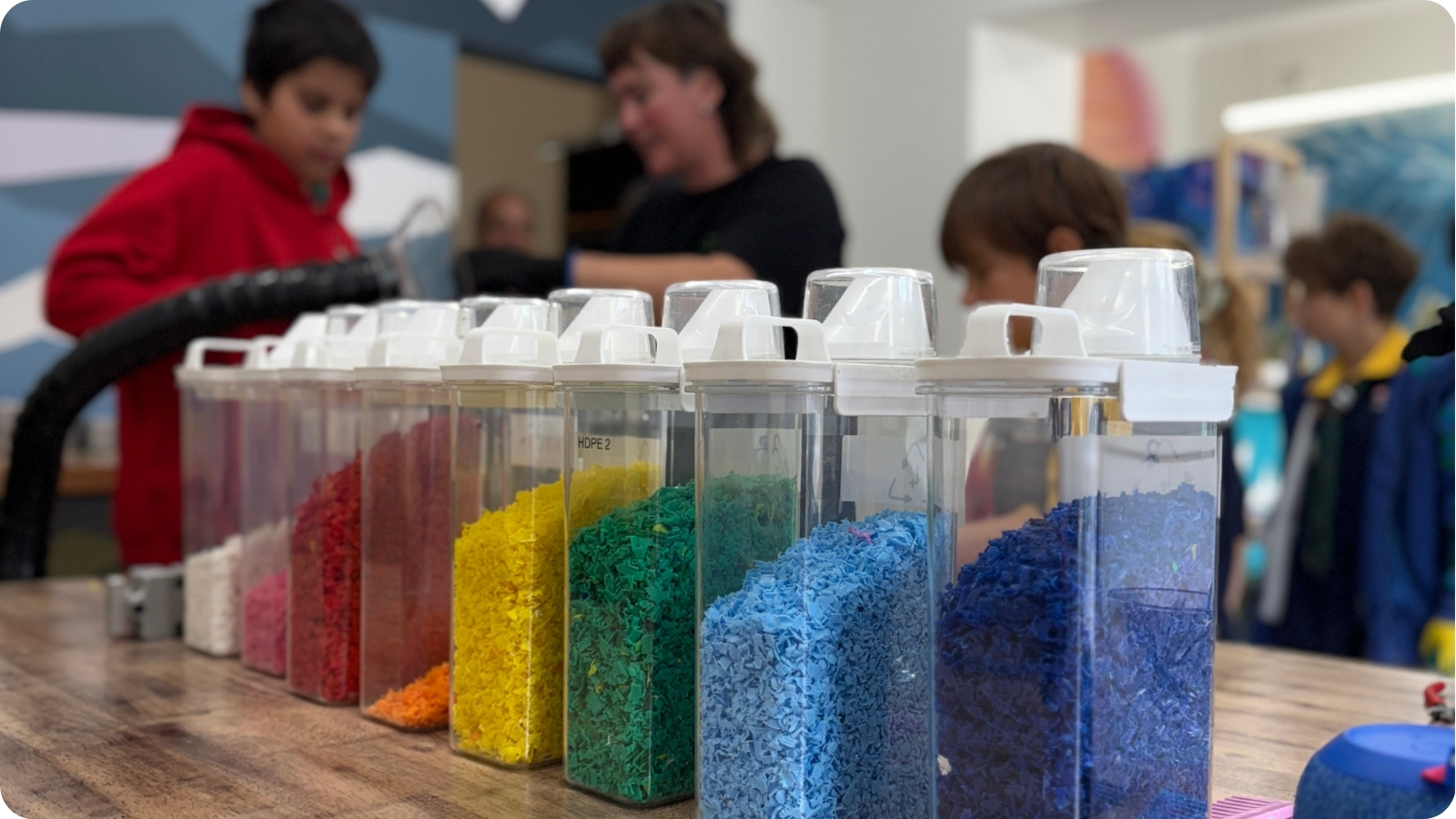 Children watching recycled plastic granules being sorted at a Reshaping Waste workshop.