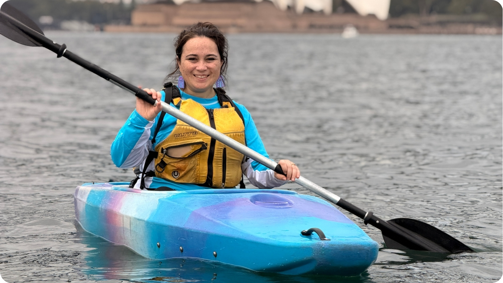 Shona paddling a kayak on Sydney Harbour in a yellow life jacket.